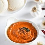 Spicy garlic chutney in a bowl topped with seasoning, curry leaves and Idlies kept behind