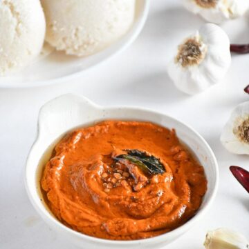 Spicy garlic chutney in a bowl topped with seasoning, curry leaves and Idlies kept behind
