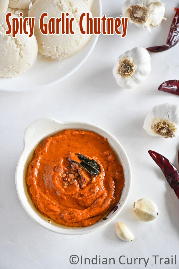 Top view of poondu kara chutney with curryleaves, idlies and garlic are kept aside.