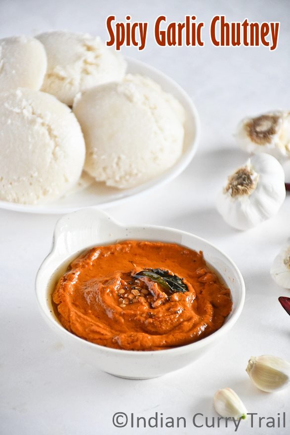 Poondu kara chutney in a bowl topped with seasoning, curry leaves and Idlies kept behind