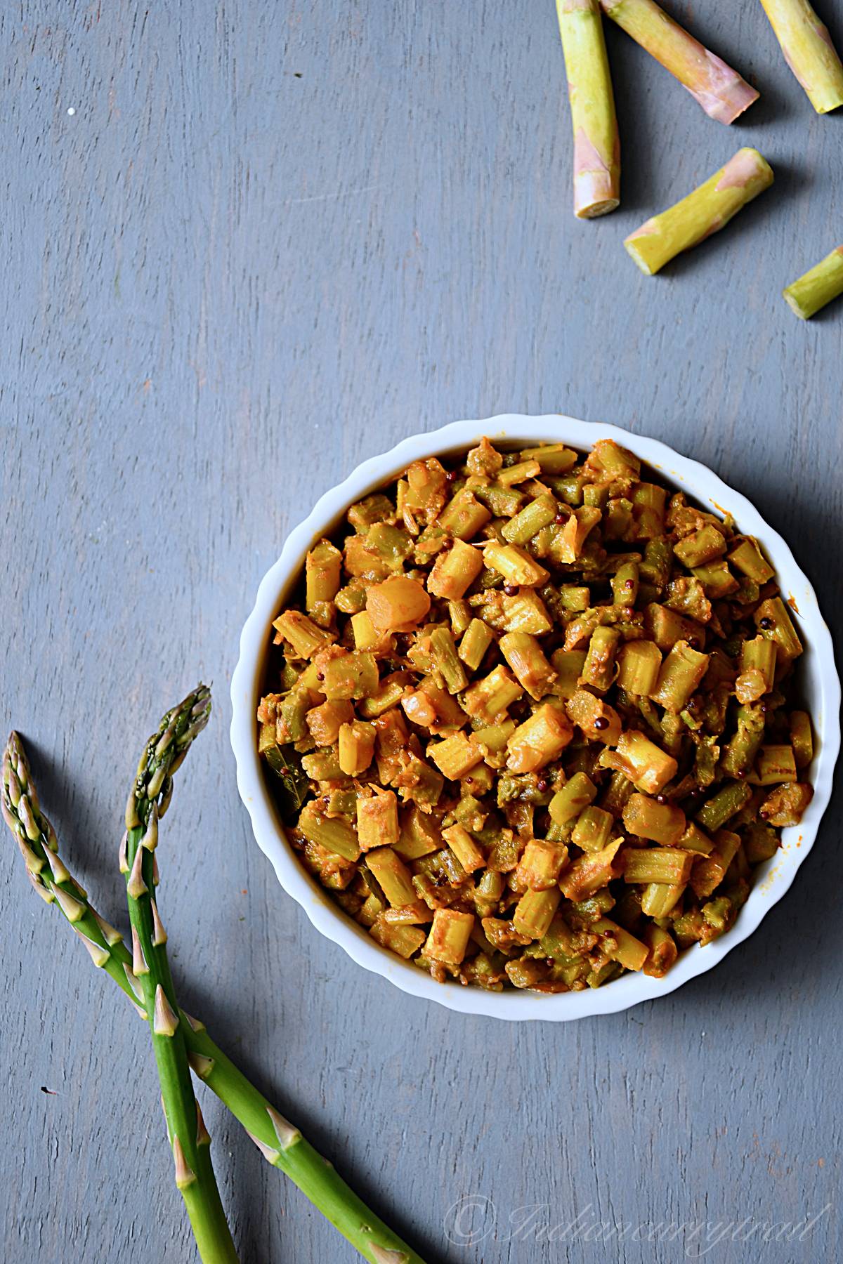 asparagus masala served in a bowl showcased near a pair of raw asparagus