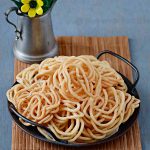 a serving tray full of urad dal murukkus with small flower vase behind