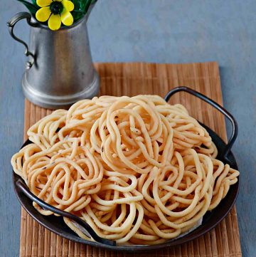 a serving tray full of urad dal murukkus with small flower vase behind