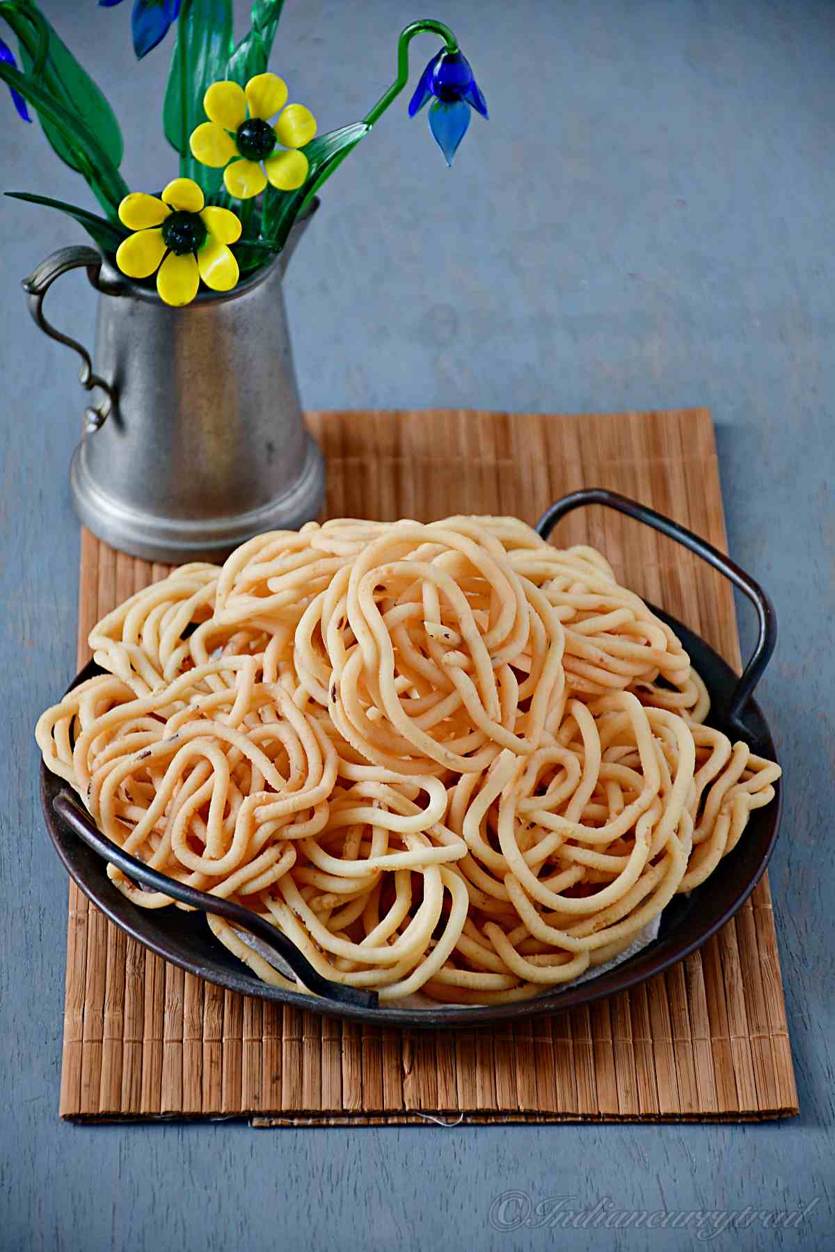a serving tray full of urad dal murukkus with small flower vase behind