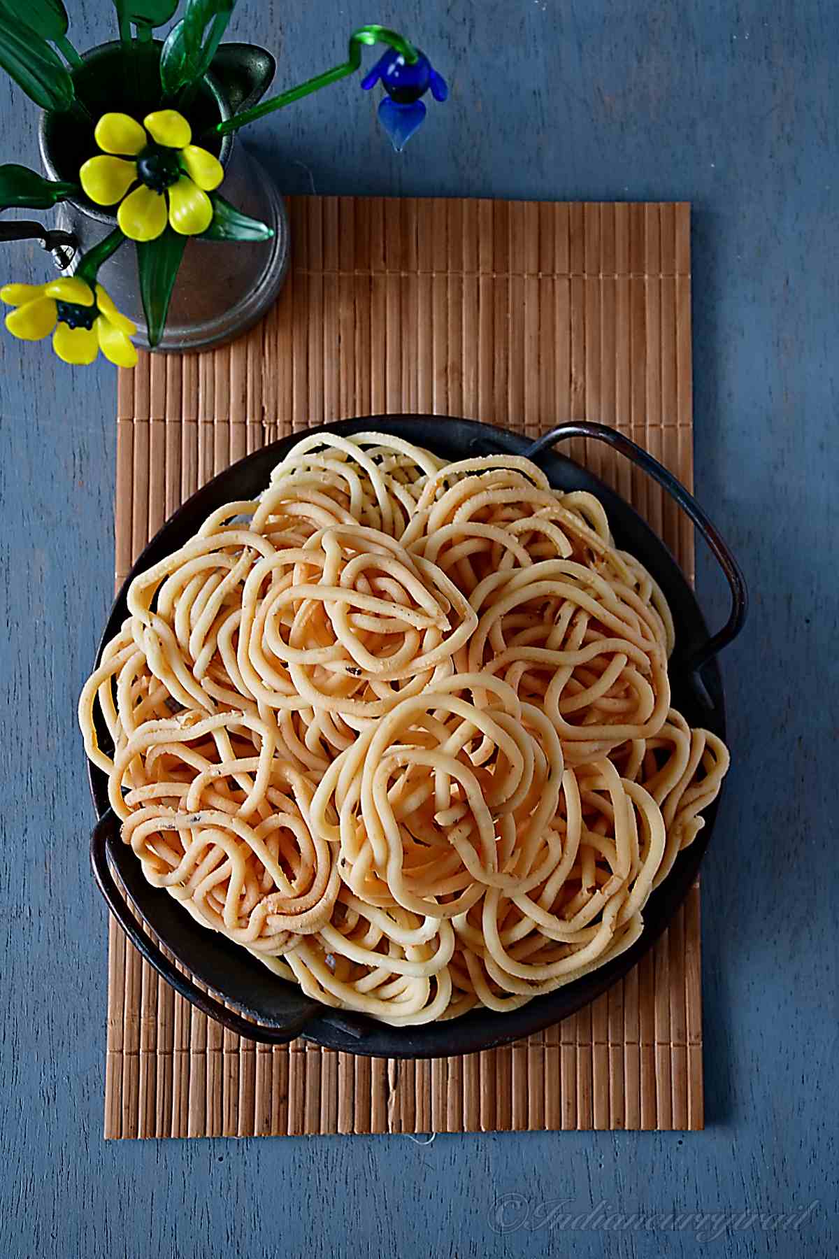 top view of urad dal murukkus arranged on serving tray with a flower vase.
