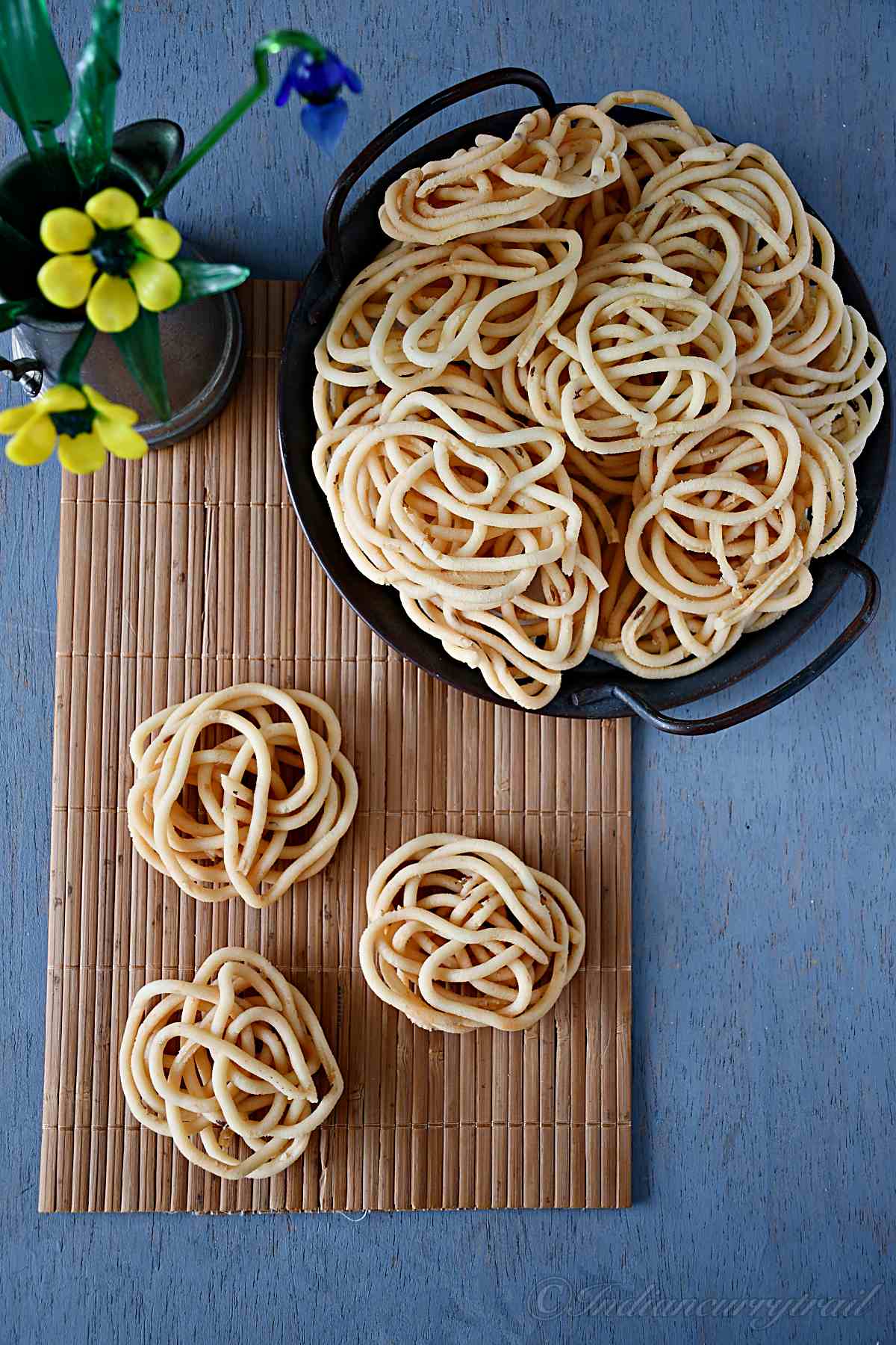 top view of three urad dal murukkus and a stack of murukkus kept on a serving tray with flower vase