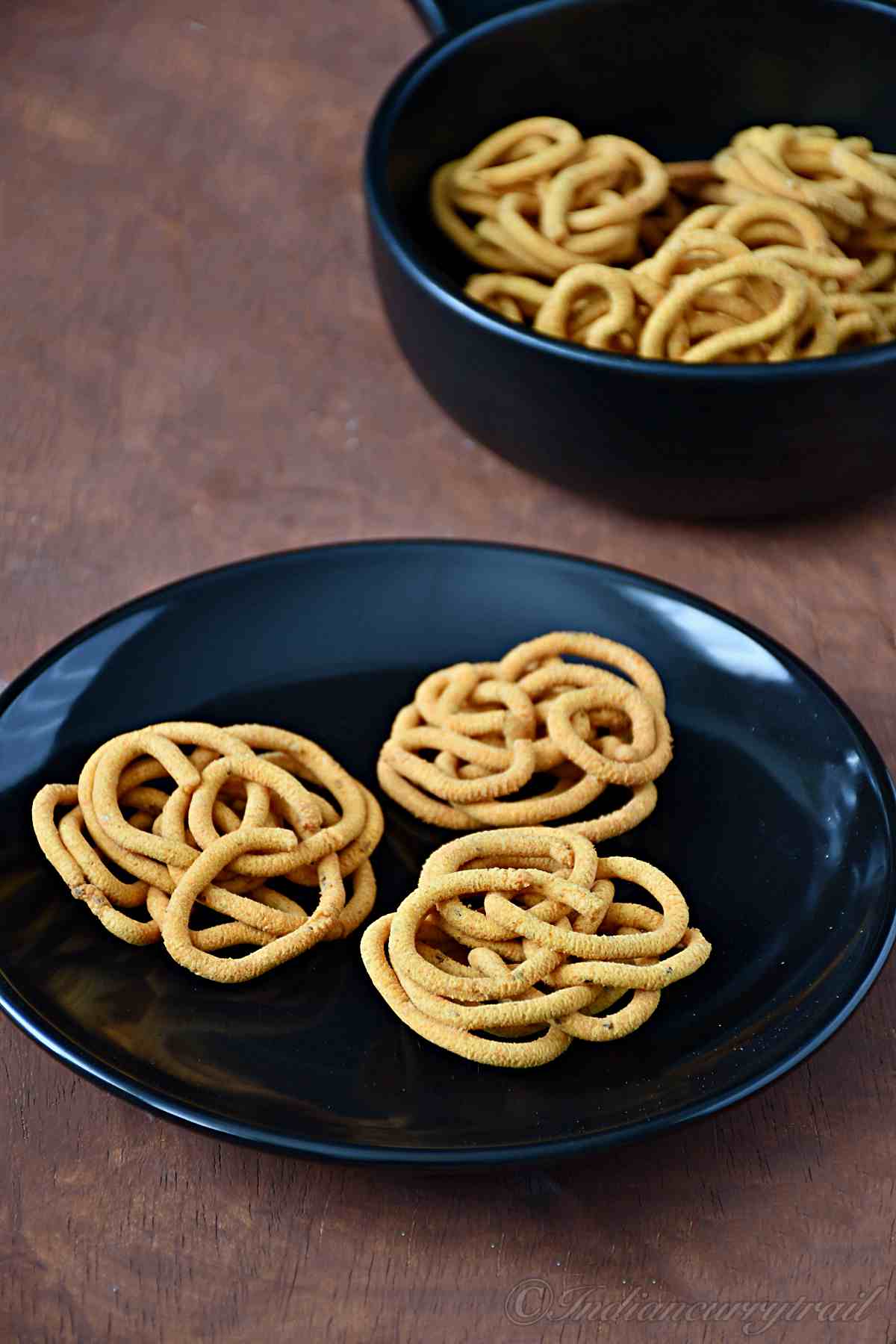 table view of besan murukku on a plate with bowl of murukkus behind