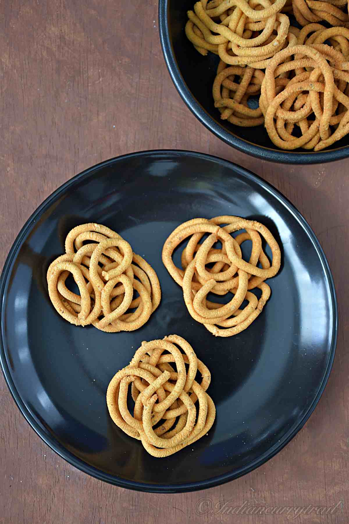 top view of gram flour murukkus on a plate with bowl of murukkus behind