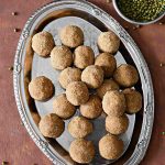 overhead shot of green moong dal laddus on a plate with a bowl of green moong dal kept aside.