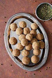 overhead shot of green moong dal laddus on a plate with a bowl of green moong dal kept aside.