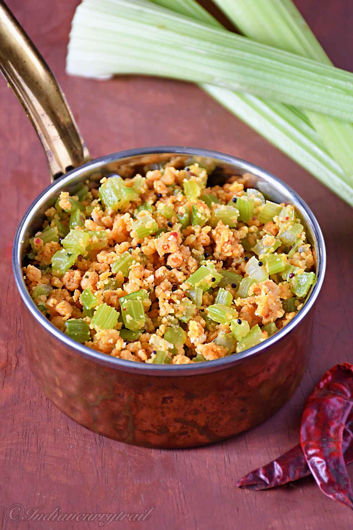 picture of celery paruppu usili with mustard seeds in a small serving bowl with dry red chilli and celery sticks aside