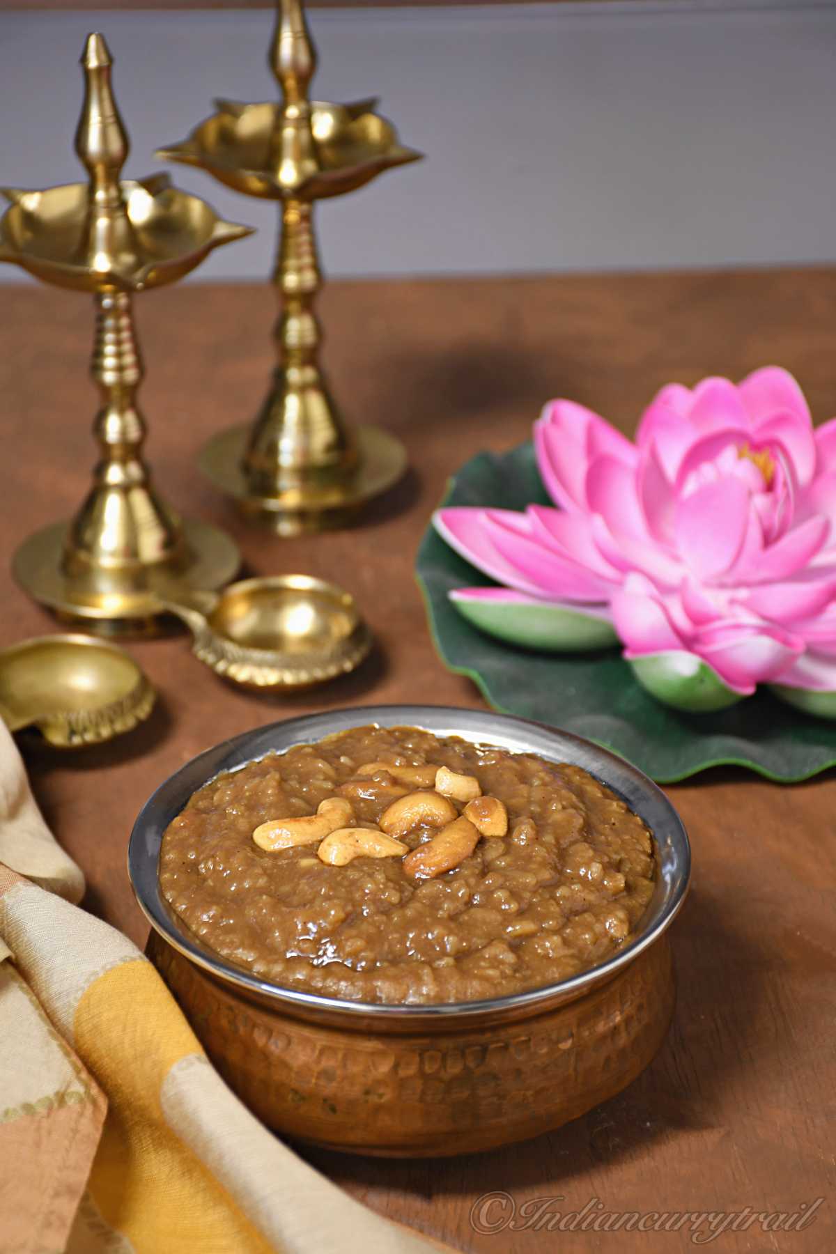 side view of gooey karupatti pongal with fried golden brown cashews on top and indian diya and lotus behind