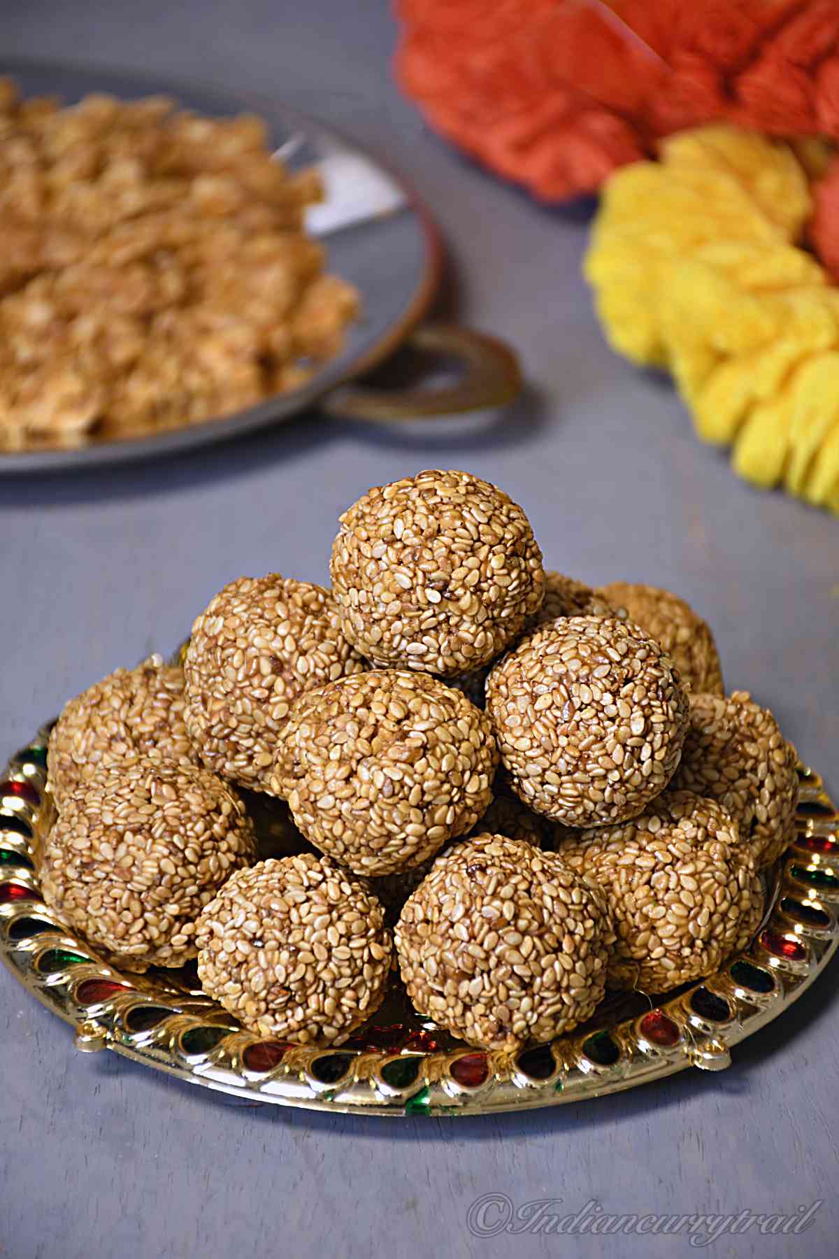 sesame seeds laddus stacked on a decorative plate with a garland and plate of jaggery behind