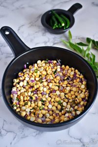 a black bowl of roasted gram dal salad mixed with finely chopped shallots and garnished with green chilli and fresh curry leaves