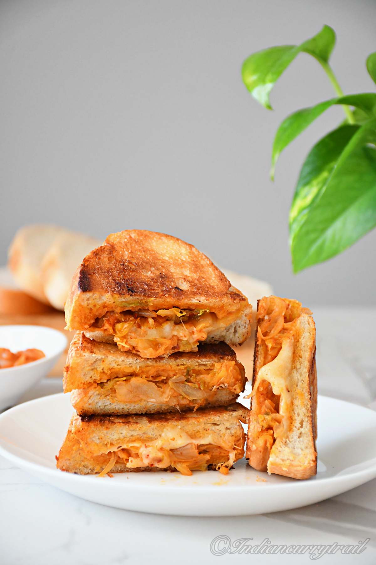 a close-up look of a stack of kimchi grilled cheese sandwiches kept on the plate where the cheese oozing out of the bread
